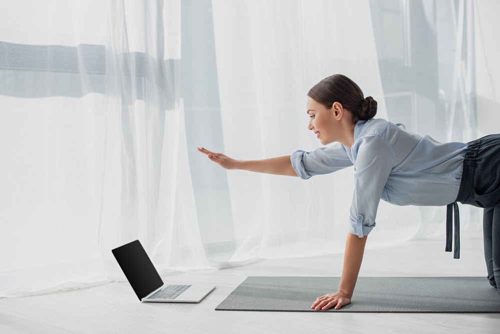 Frau macht Yoga und schaut auf ihren Laptop